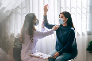 Doctor assessing woman with difficulty raising stiff shoulder overhead